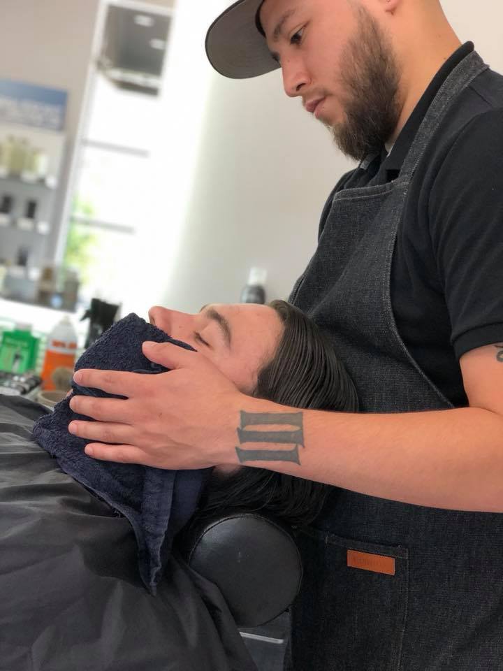 Barber placing a warm towel on a relaxed male client's face in a barbershop. - K. Charles & Co. in Schertz, TX