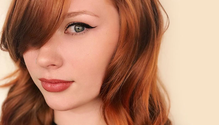 Close-up of a young woman with red hair styled from a salon, a nose piercing, and winged eyeliner, looking at the camera with her head slightly tilted. - K. Charles & Co. in Schertz, TX