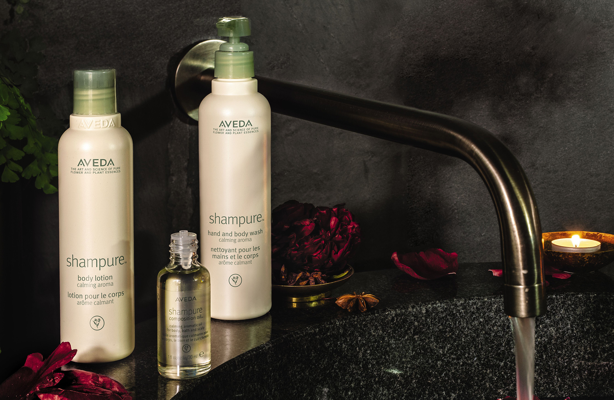 Two aveda shampure products on a dark bathroom counter with a faucet, rose petals, and a lit candle in the background. - K. Charles & Co. in Schertz, TX