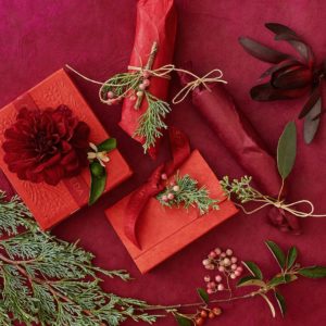Gift boxes wrapped in red paper with natural decorations like pine branches and a red flower on a deep red background. - K. Charles & Co. in Schertz, TX
