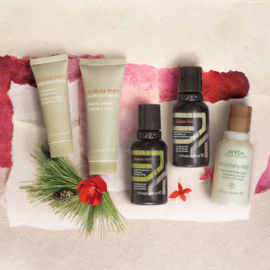 Assortment of aveda skincare products displayed on a textured paper background with pine needles and a red flower accent. - K. Charles & Co. in Schertz, TX