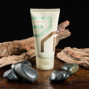 A tube of cosmetic cream on a dark surface, flanked by smooth dark stones and pieces of wood, against a black background. - K. Charles & Co. in Schertz, TX