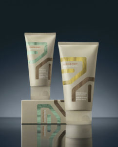 Two tubes of cosmetic cream with modern design, standing upright in front of a muted blue background, one partially behind the other. - K. Charles & Co. in Schertz, TX