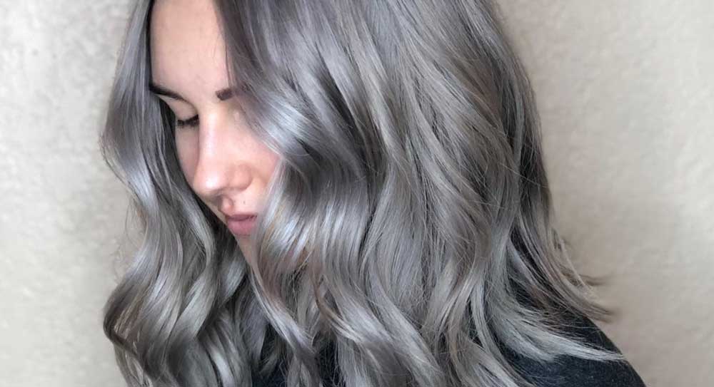 A woman with long, wavy silver hair styled at a salon looking downward. - K. Charles & Co. in Schertz, TX
