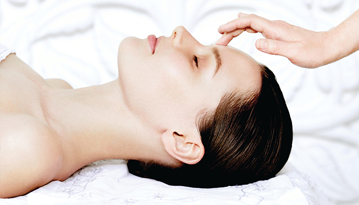 A woman receiving a facial treatment with a hand applying product to her forehead in a serene, spa-like setting, while her hairstyle is elegantly arranged to highlight the relaxation process. - K. Charles & Co. in Schertz, TX