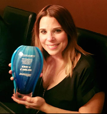 Woman smiling, holding a blue award with "premios juventud" and names "erika y carlos" inscribed on it. - K. Charles & Co. in Schertz, TX