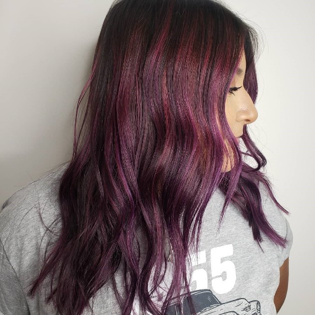 Side profile of a person with long, wavy hairstyle dyed in shades of purple and burgundy, wearing a grey t-shirt. - K. Charles & Co. in Schertz, TX