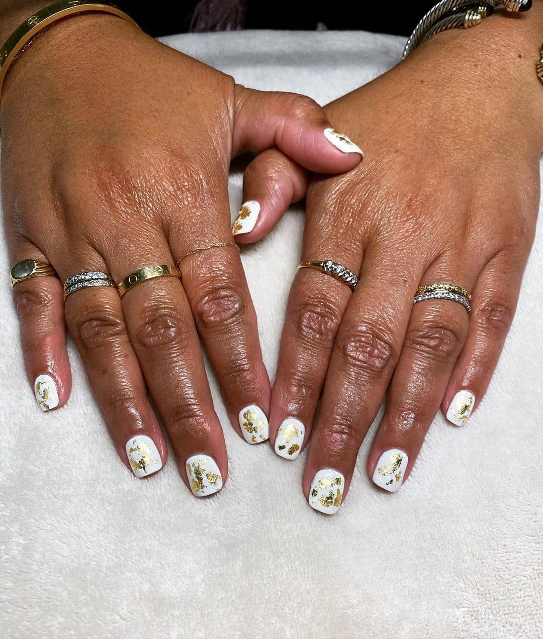 Two hands with long, manicured nails featuring white polish and floral designs, adorned with multiple rings on the fingers, resting on a white surface. - K. Charles & Co. in Schertz, TX