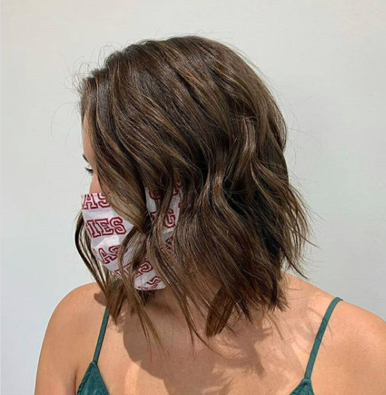 Woman with a medium-length wavy brown hairstyle wearing a mask with red text design, facing away from the camera against a plain background. - K. Charles & Co. in Schertz, TX