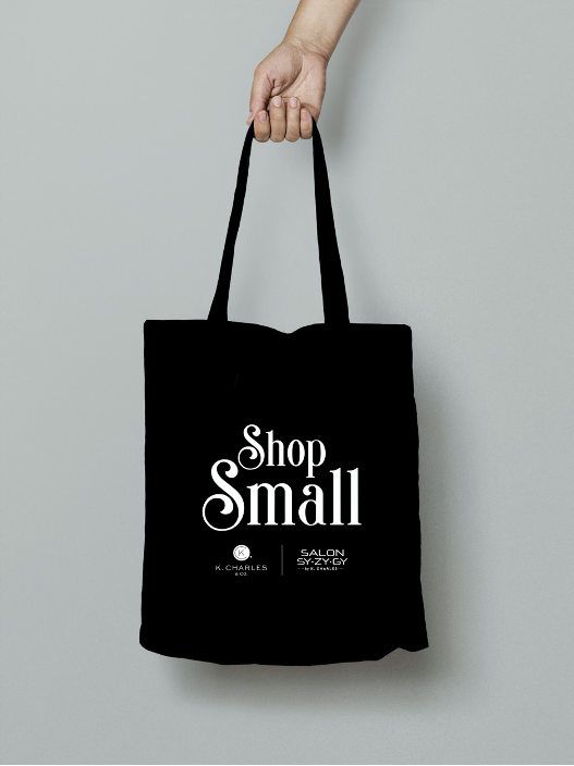 A hand holding a black tote bag with the logo "salon" printed in white along with additional text and a graphic. - K. Charles & Co. in Schertz, TX