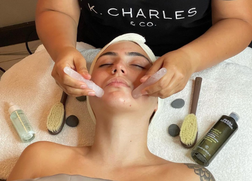 A person receiving a facial treatment with their eyes covered, as a therapist applies tools and products on their face in a salon setting. - K. Charles & Co. in Schertz, TX
