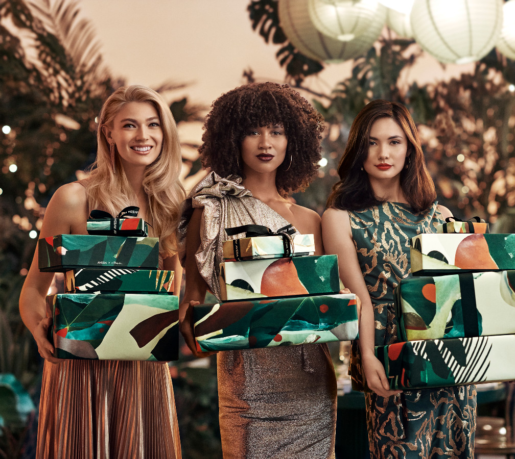 Three women holding gift boxes at a festive outdoor party, smiling and dressed in elegant evening wear. - K. Charles & Co. in Schertz, TX