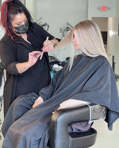 Hair stylist in a mask creating a new hairstyle for the blonde hair of a female client in a salon. - K. Charles & Co. in Schertz, TX