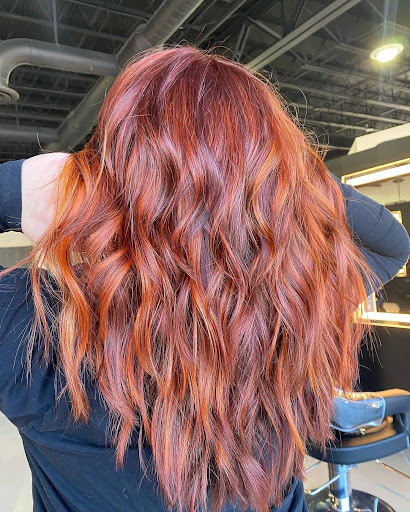 A woman with long, wavy auburn hair color, viewed from behind, in a salon setting. - K. Charles & Co. in Schertz, TX