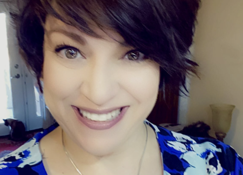 A woman with a stylish short hairstyle and a blue floral top smiling warmly at the camera, with a softly blurred background. - K. Charles & Co. in Schertz, TX