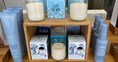 A display of Aveda beauty products including candles, hair sprays, and lotions arranged on wooden shelves in a salon. - K. Charles & Co. in Schertz, TX