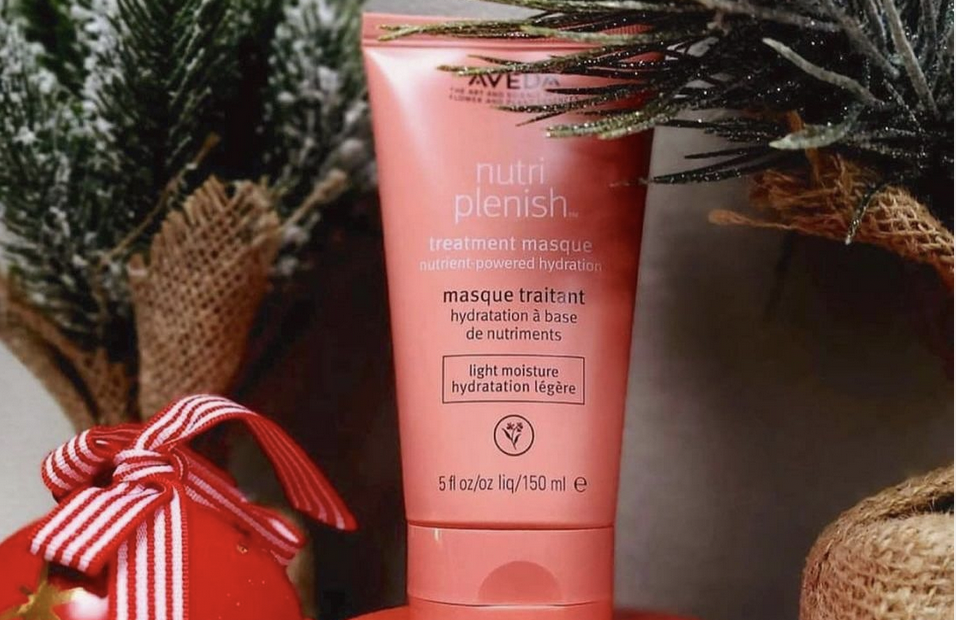Aveda nutriplenish treatment masque tube beside a Christmas ornament and pine branches, promoting holiday hair color. - K. Charles & Co. in Schertz, TX