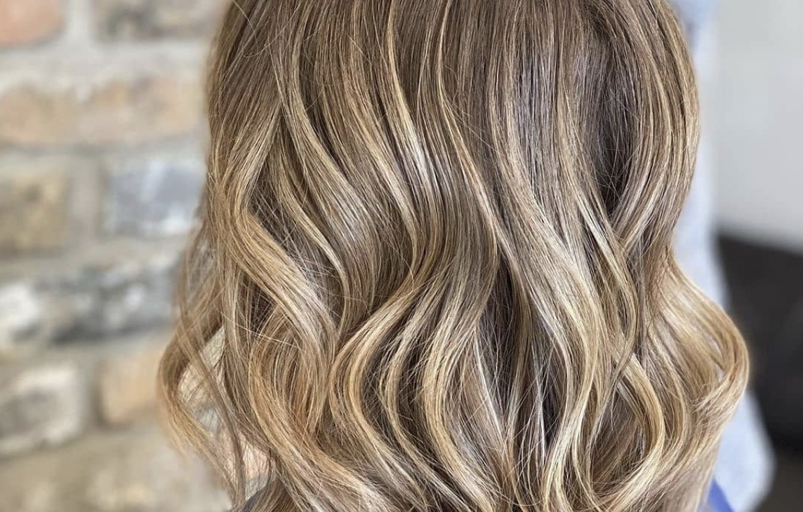 Close-up of a woman's hairstyle showcasing soft, cascading curls with blended brunette and blonde highlights. - K. Charles & Co. in Schertz, TX