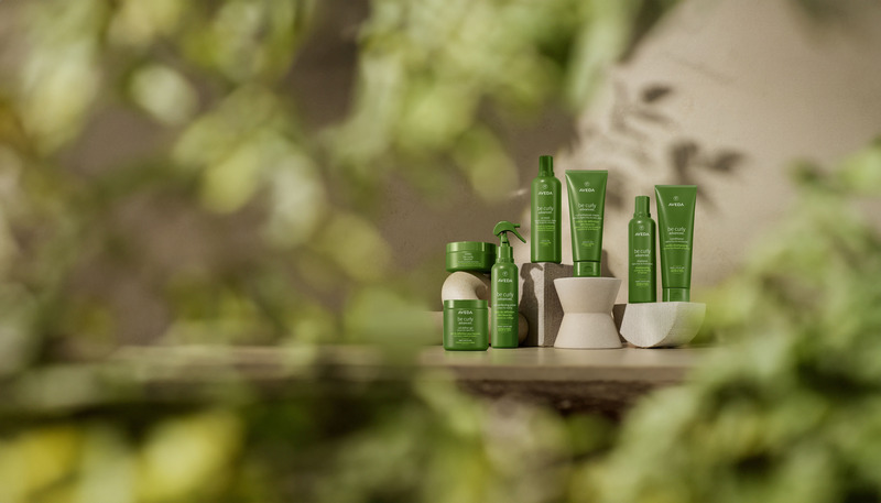 A collection of green skincare products arranged neatly on a reflective surface with a blurred green foliage background. - K. Charles & Co. in Schertz, TX