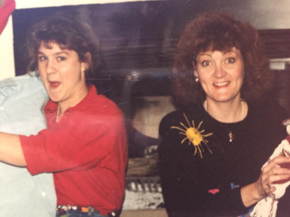 Two women in a kitchen, one playfully dancing with an apron and the other holding a doll, both smiling, with a homey backdrop. - K. Charles & Co. in Schertz, TX