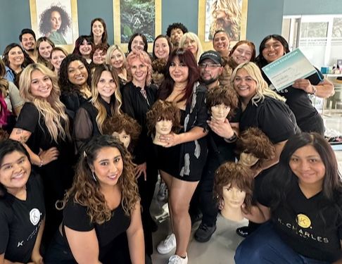 A group of people, mostly women, smile while holding mannequin heads with various hairstyles. They appear to be in a salon or cosmetology training setting. - K. Charles & Co. in Schertz, TX