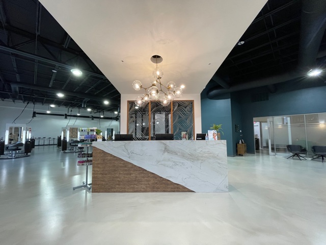 A modern salon reception area with a marble counter, contemporary chandelier, retail display on the left, and seating areas in the background. - K. Charles & Co. in Schertz, TX
