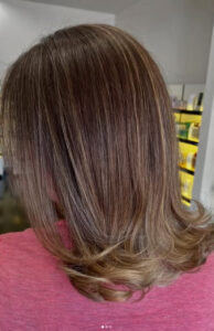 Person with shoulder-length, straight light brown hair with subtle blonde highlights, wearing a pink top, shown from the back in an indoor setting. - K. Charles & Co. in Schertz, TX