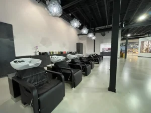 A row of black salon shampoo chairs with sinks in a modern, minimalist hair salon featuring pendant lights and a polished concrete floor. - K. Charles & Co. in Schertz, TX