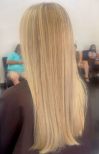 A person with straight, long, blonde hair is seated indoors, with several people sitting in chairs in the background. - K. Charles & Co. in Schertz, TX